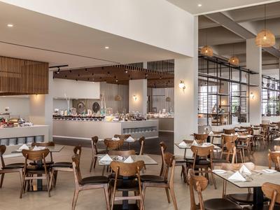 Modernes Hotelrestaurant mit Holzstühlen, beigen Tischen und großem Buffetbereich.