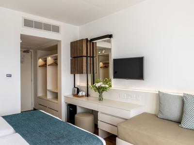 Helles Hotelzimmer mit Bett, Sofa, Schreibtisch, Spiegel und Fernseher.