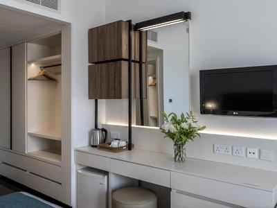 Moderner Hotelzimmerbereich mit Wandfernseher, Spiegel, Schreibtisch und offenem Kleiderschrank.
