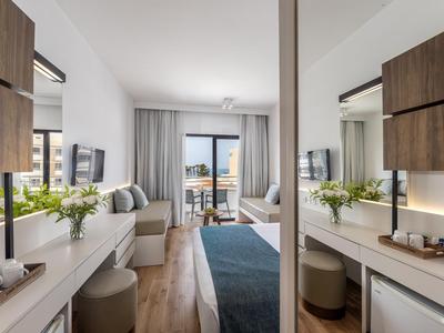 Modern eingerichtetes Hotelzimmer mit Sitzbereich, großem Fenster und Balkon mit Meerblick.
