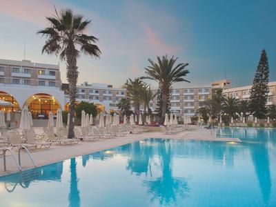 Grand piscine d'hôtel avec palmiers et transats au coucher du soleil