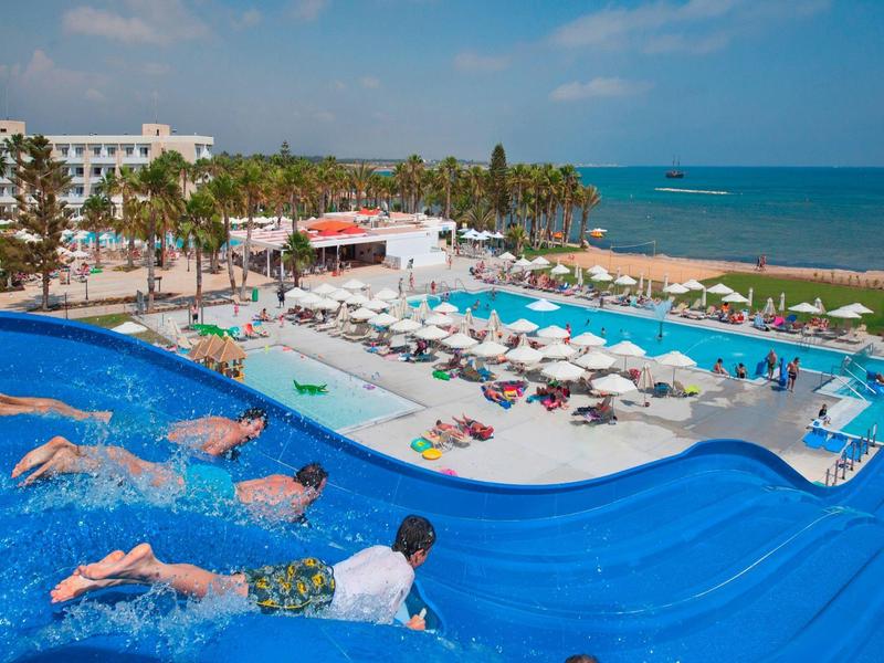 Großer blauer Wasserrutschenbereich mit mehreren Becken, Sonnenschirmen und Blick auf das Meer.