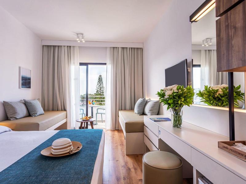 Moderner Wohnraum mit Sofas, Teppich, TV, Tisch, Blumen und Blick auf Balkon mit grüner Landschaft.