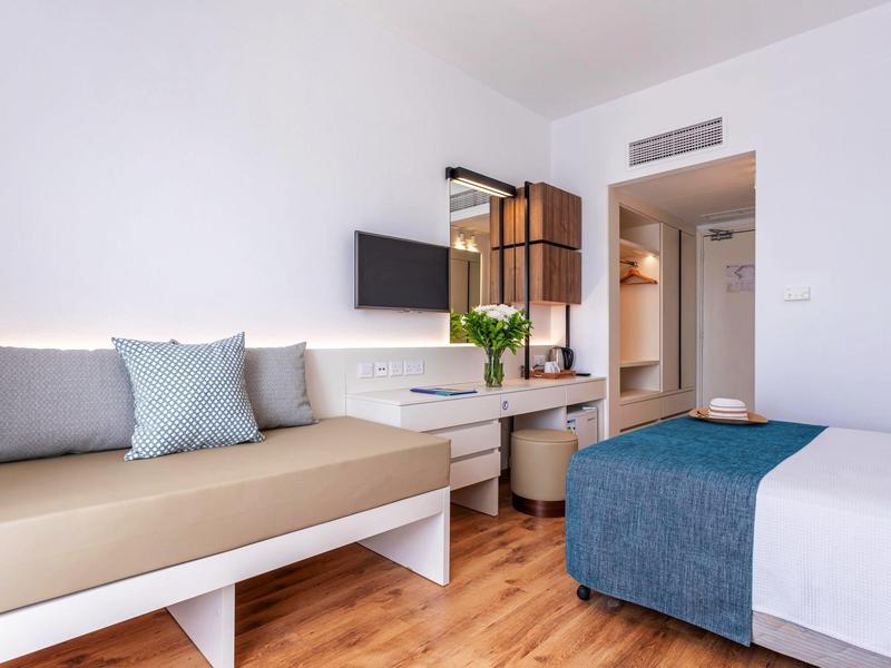 Modernes Schlafzimmer mit Holzfußboden, weißem Mobiliar, grauen Kissen und einem blauen Bettüberwurf.