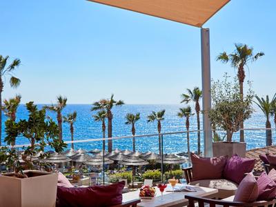 Terrasse mit Sitzbereich und Blick auf das Meer und Palmen bei klarem Himmel.