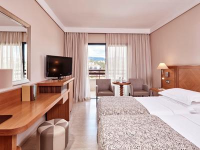 Modernes Hotelzimmer mit zwei Einzelbetten, Fernseher, Schreibtisch und Balkon mit Ausblick.