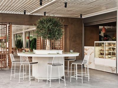 Moderner Essbereich mit rundem weißem Tisch, hohen Stühlen und Blick auf eine Vitrine mit Backwaren.