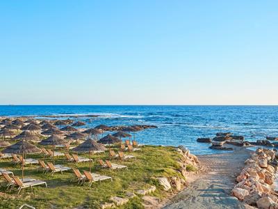 Strand mit vielen Sonnenschirmen, Liegestühlen und einem Weg aus Steinen zum Meer.