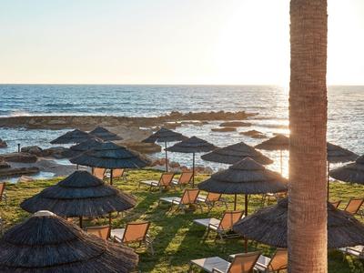 Sonnenuntergang am Strand mit Liegestühlen und Strohmsonnenschirmen am Wasser
