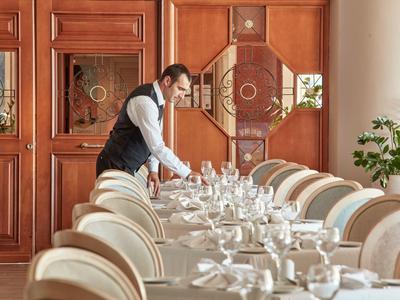 Ein Kellner richtet einen lang gedeckten Tisch in einem eleganten Speisesaal mit Holzverkleidung ein.