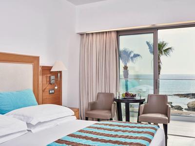 Hotelzimmer mit Doppelbett, Sitzecke und Blick auf das Meer durch eine Glasschiebetür.