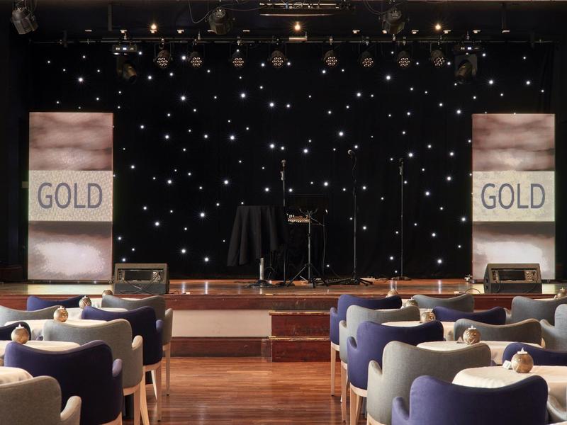 Bühne mit Mikrofon und Lautsprechern vor Sitzreihen in einem Veranstaltungsraum.