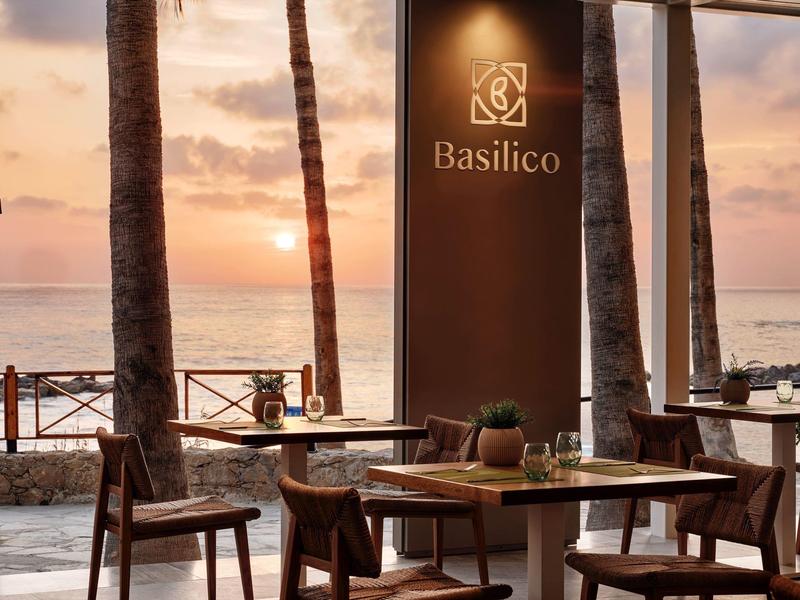 Restaurantterrasse mit Holztischen und Stühlen am Meer bei Sonnenuntergang