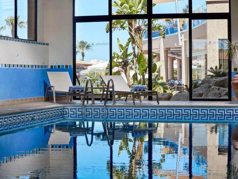 Innenpool mit großen Fenstern und Blick auf Palmen und Außenbereich