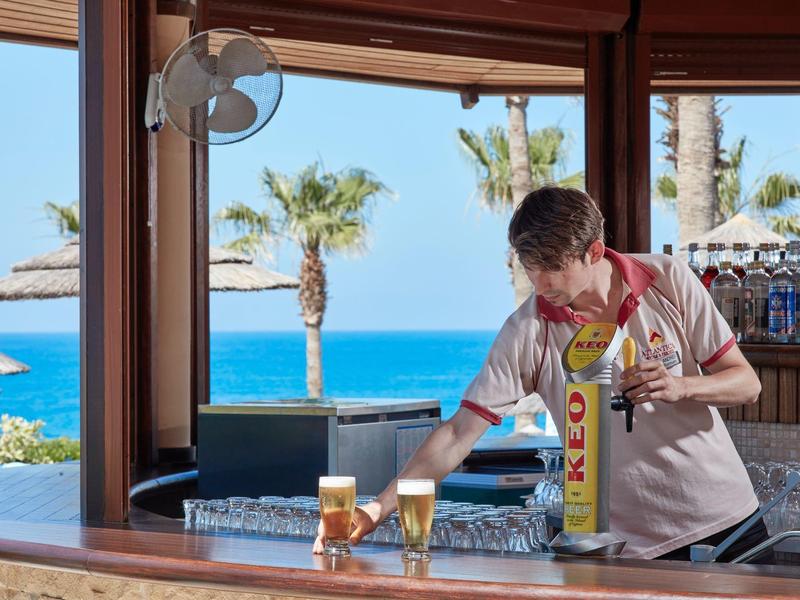 Barkeeper serviert zwei Gläser Bier an einer Hotelbar mit Meerblick und Palmen.