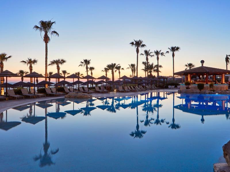 Blick auf einen ruhigen Hotelpool mit Palmen und Liegestühlen bei Sonnenuntergang.
