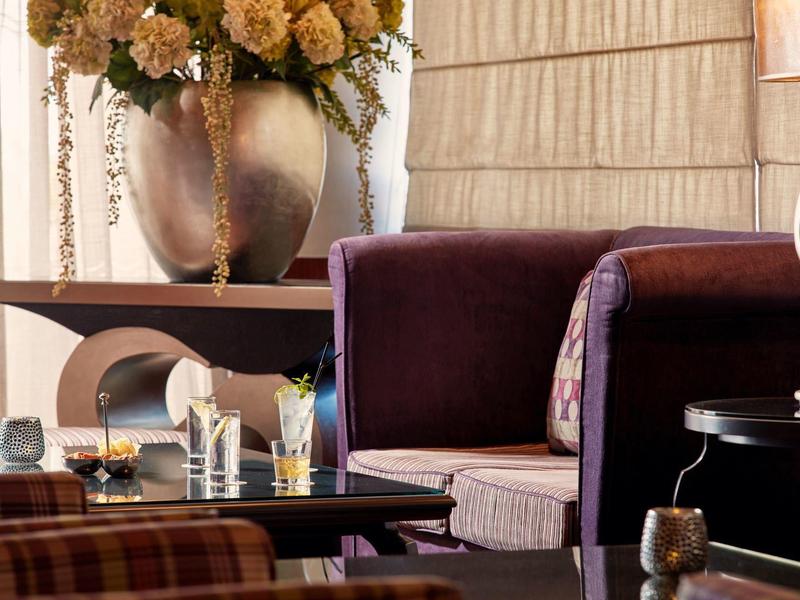 Elegante Hotellounge mit violetten Sesseln, Blumenarrangement und stilvollen Tischen.