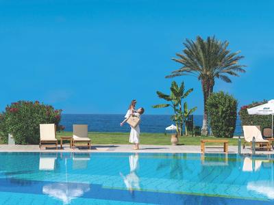 Schwimmbad mit blauer Wasserfläche, Liegestühlen, Palmen und Blick aufs Meer.