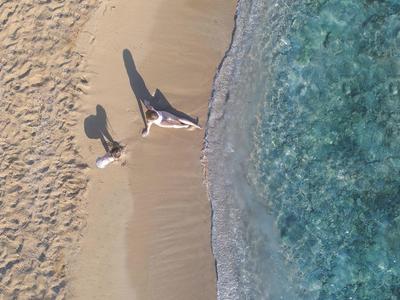 Zwei Personen liegen am sandigen Strand neben klarem, blauem Wasser mit sanften Wellen.