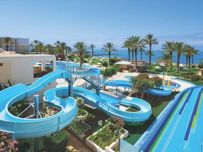 Großer Wasserpark mit blauen Wasserrutschen, Palmen und Blick auf das blaue Meer im Hintergrund.