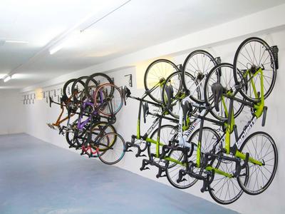 Biciclette appese ordinatamente a supporti a muro in una stanza interrata bianca e luminosa.