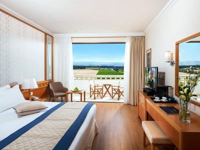 Camera d'hotel luminosa con letto matrimoniale, pavimento in legno e balcone con vista mare.