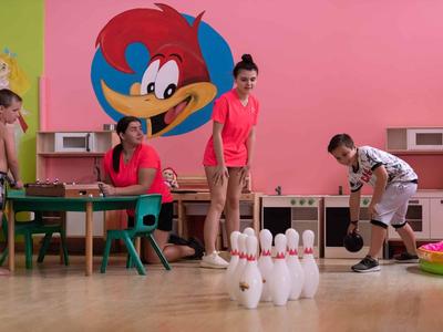 Bambini che giocano a bowling in un'area interna colorata con una grande immagine di cartone animato sul muro.