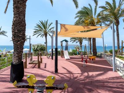 Area giochi per bambini con scivolo e tenda parasole sulla spiaggia con palme e vista mare