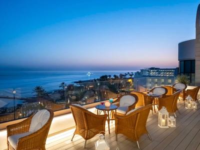 Terrazza con sedie di vimini e tavoli con vista sul mare al tramonto.