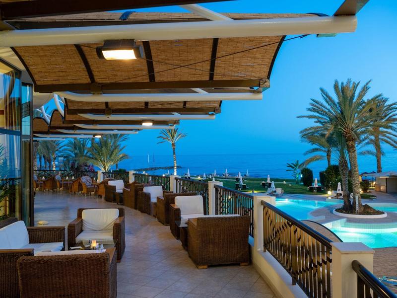 Terrassenlounge mit Rattansesseln, beleuchtetem Whirlpool und Palmenblick bei Abenddämmerung.