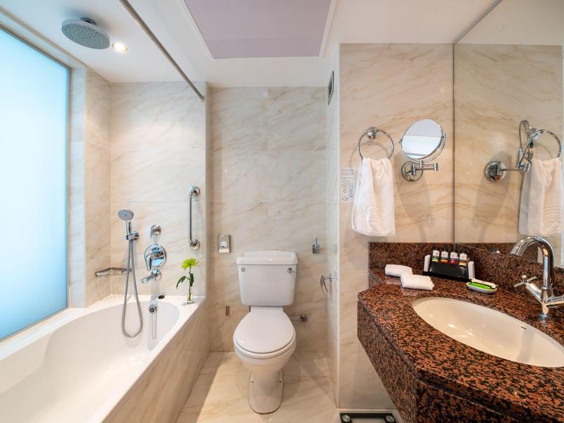 Moderne Badezimmereinrichtung mit Badewanne, Toilette, Marmorfliesen und großem Spiegel.