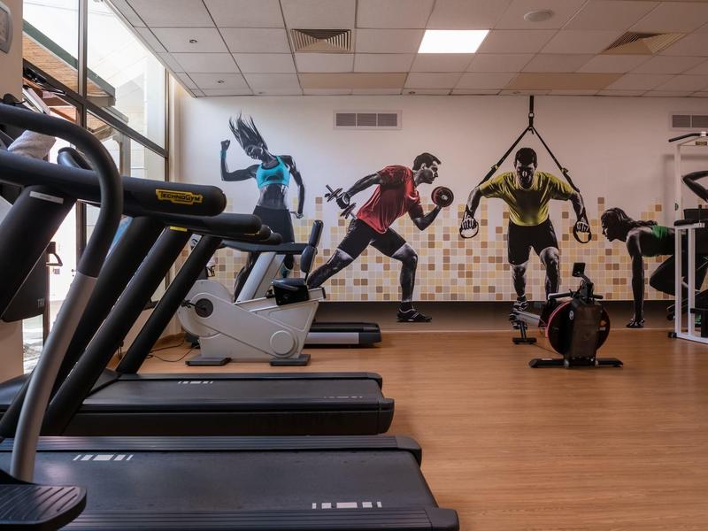 Fitnessraum mit Laufbändern, Fahrrädern und zwei trainierenden Personen in Sportkleidung.