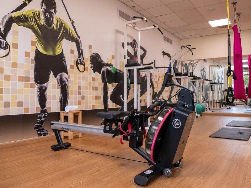 Fitnessraum mit Rudermaschine, Holzfußboden, bunten Wandgemälden und Trainingsmatten.
