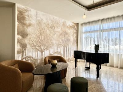 Elegante hotelruimte met bruine fauteuils, zwarte vleugel en groot muurschildering van bomen.