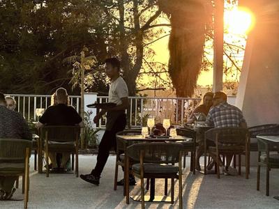 Gastheer serveert drankjes op terras bij zonsondergang in een ontspannen sfeer.