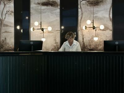 Empfangstresen mit dunklem Holz, zwei Bildschirmen, modernem Leuchtdesign und großem Natur-Wandbild.