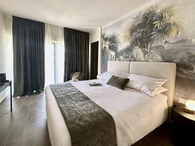 Moderne hotelkamer met groot bed, donkere gordijnen en tropisch muurschildering.