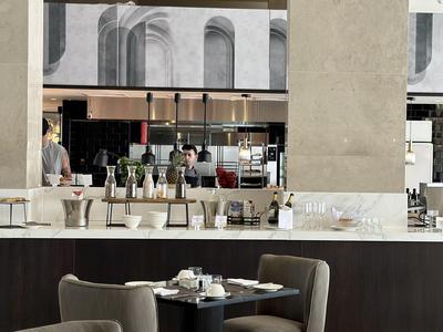 Modern cafégebied in een hotel met tafels, stoelen en een bar op de achtergrond.