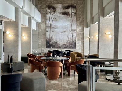 Moderne hotel lounge met comfortabele stoelen en een grote muurschildering in neutrale tinten.