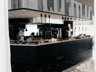 Moderne schwarze Kücheninsel mit Holzarbeitsplatte, eingebauten Geräten und Hängelampen in heller Küche.