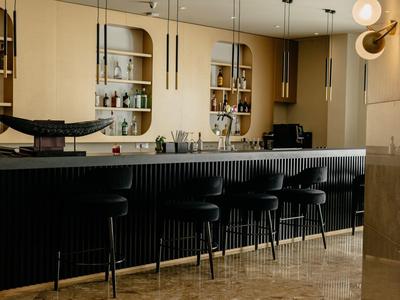 Moderner Barbereich mit schwarzer Theke, hohen Stühlen, Regalen und warmem, gedämpftem Licht.