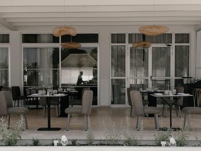 Moderner Außenbereich eines Cafés mit grauen Stühlen, runden Tischen und großen Fenstern.