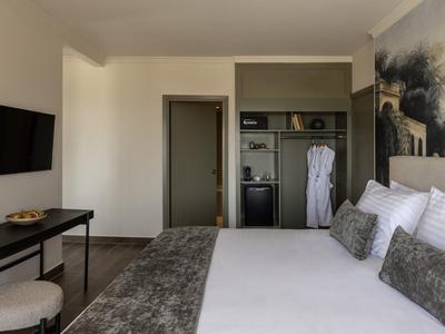 Modernes Hotelzimmer mit großem Bett, grauen Kissen, TV und offener Garderobe.