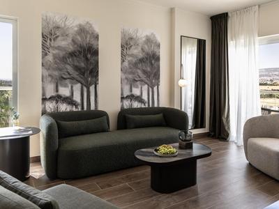 Modern eingerichtetes Hotelzimmer mit Sofa, Sesseln und großen Waldbildern an der Wand.