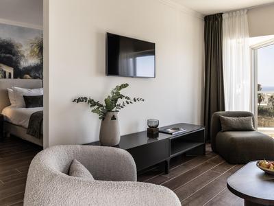 Moderner Hotel-Wohnbereich mit Sesseln, TV, Dekoration und Zugang zu einem Balkon mit Meerblick.