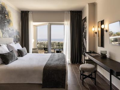 Modernes Hotelzimmer mit großem Bett, Schreibtisch und Blick auf Balkon und Meer.