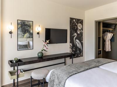 Modernes Hotelzimmer mit gemütlichem Bett, TV, Kunstwerken und offener Kleidungsgarderobe.