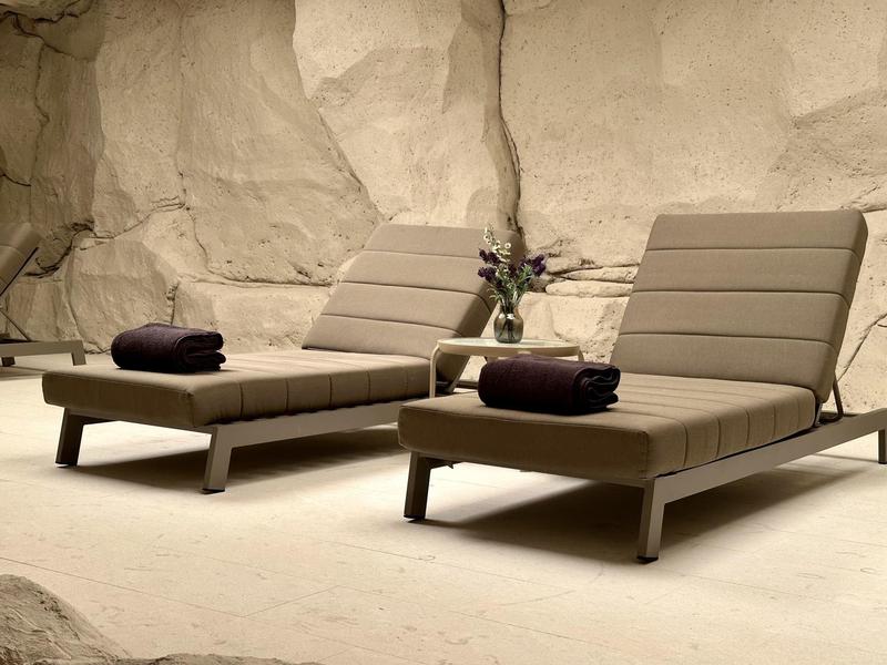 Zwei moderne graue Liegestühle vor einer rauen Felswand mit gefalteten Handtüchern und Vase.