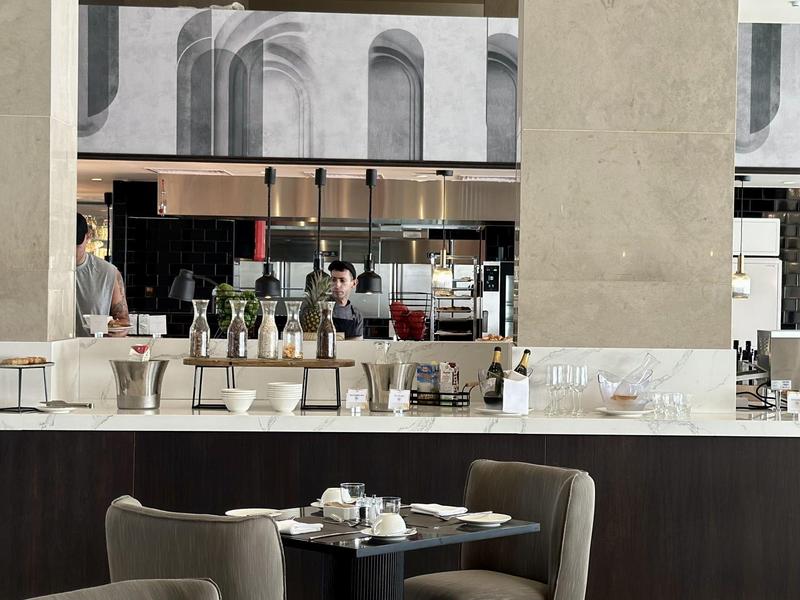 Moderne Café-Theke mit Barhockern, Pflanzen, Gläsern und einer großen Säule im Innenraum.