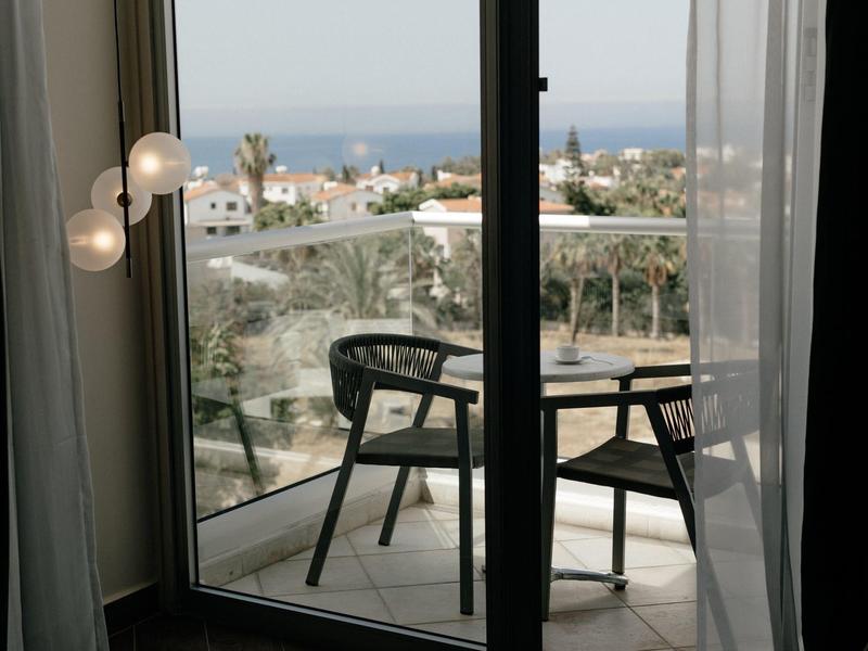 Balkon mit runden schwarzen Stühlen und Blick auf Meer und Stadt im Hintergrund bei Tageslicht.